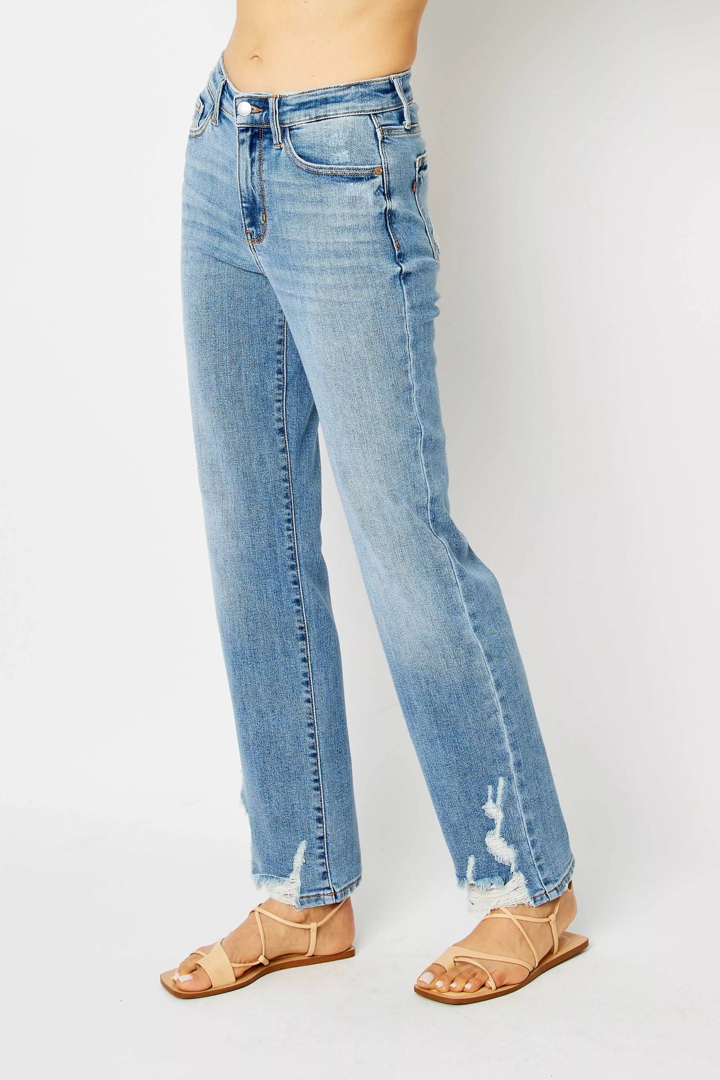 Side angle of plus size Judy Blue Estee medium wash straight jeans with raw hem and destroy.