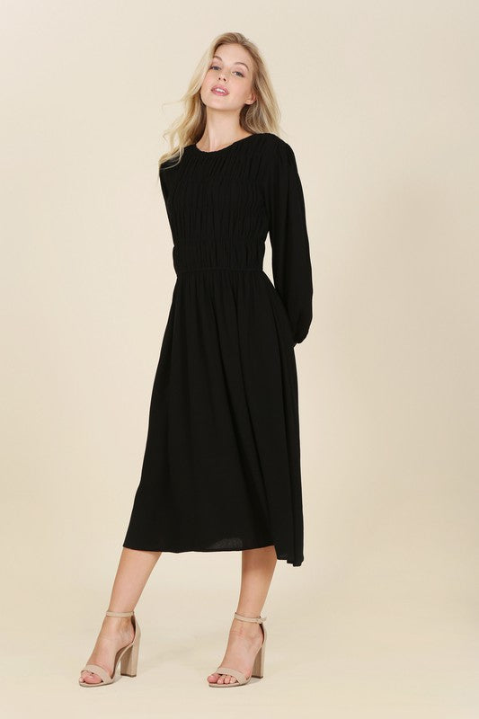 Black midi dress with a boat neck, ruched bodice, long sleeves, and buttoned cuffs. Made from crinkle fabric.