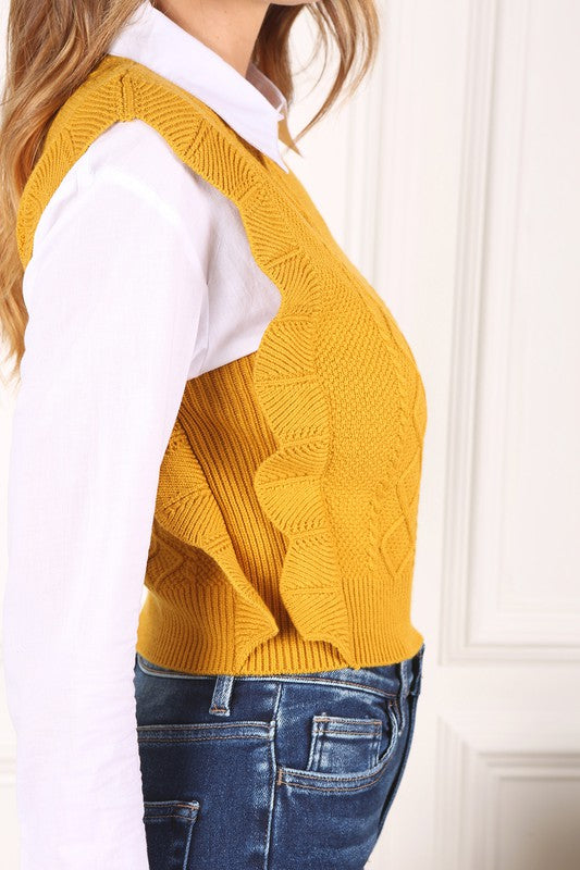 Mustard yellow sweater vest with argyle jacquard pattern, and ruffle trim on the armholes. Sleeveless with a round neckline.