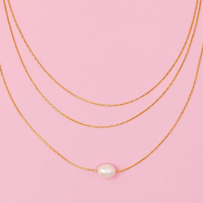 Flat lay of layered freshwater pearl pendant necklace on pink background