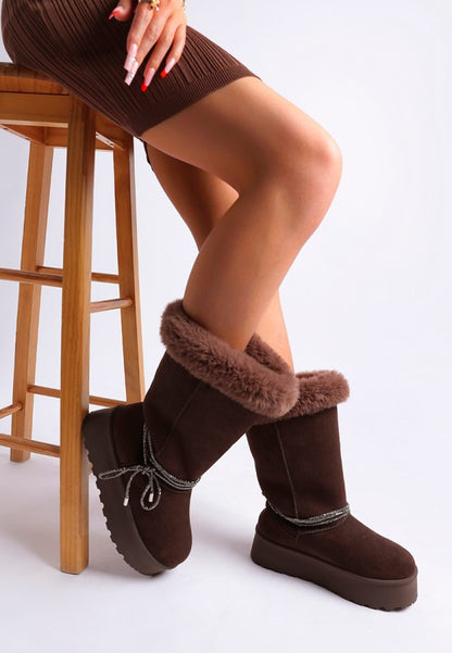 Model seated in brown snow boots highlighting plush cuff and platform sole.