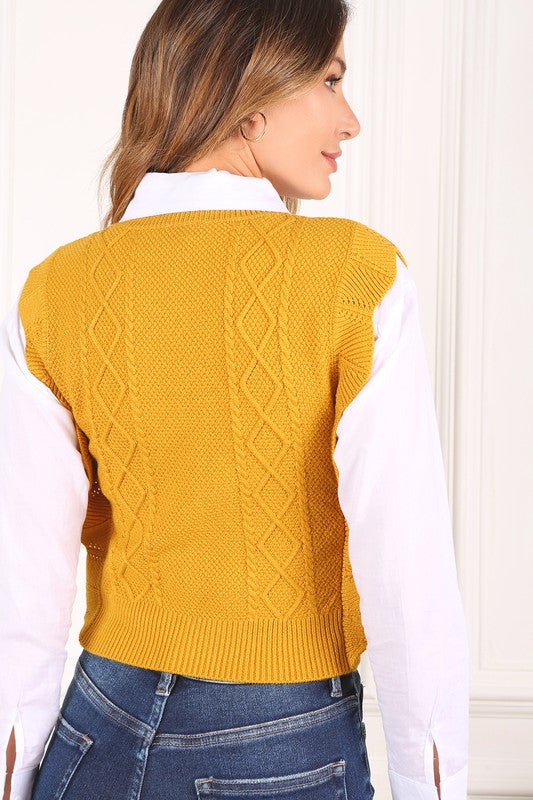 Mustard yellow sweater vest with argyle jacquard pattern, and ruffle trim on the armholes. Sleeveless with a round neckline.