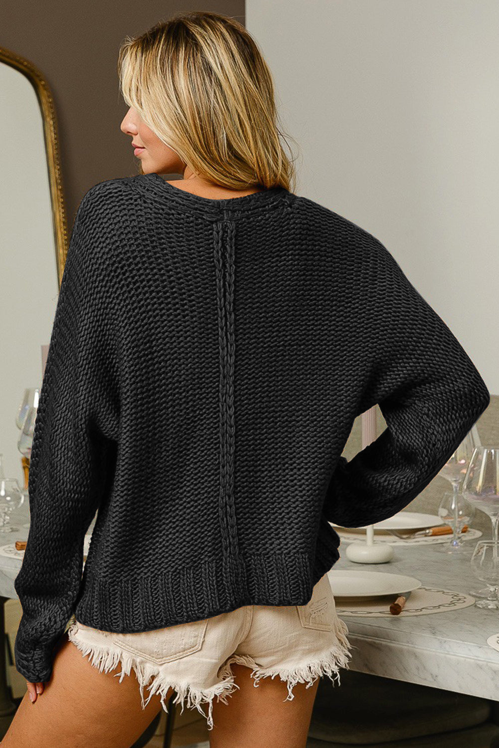 Black cable-knit sweater with long sleeves and a V-neck neckline.