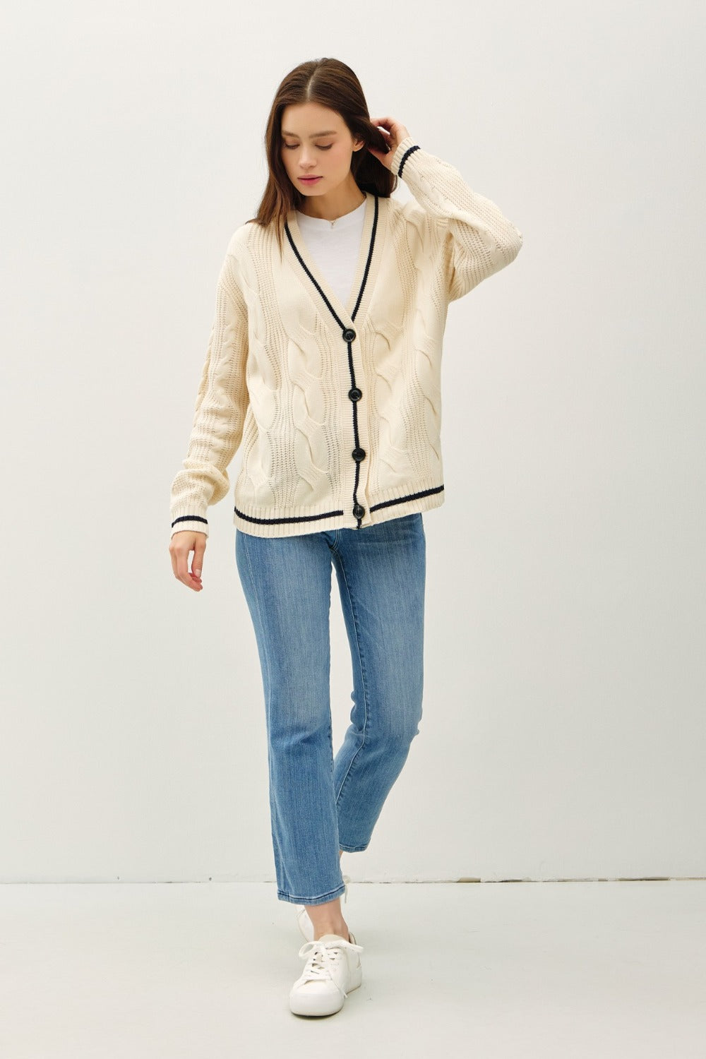 Natural and black contrast trim cable-knit cardigan with woven details and button closure.