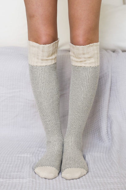 Woman standing in oatmeal Jerica Knitted Lounge Socks, oversized knee-high style.