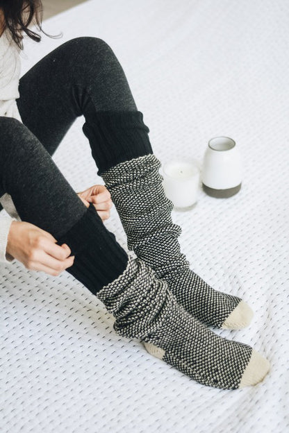 Woman sitting wearing black Jerica Knitted Lounge Socks with open-work design.