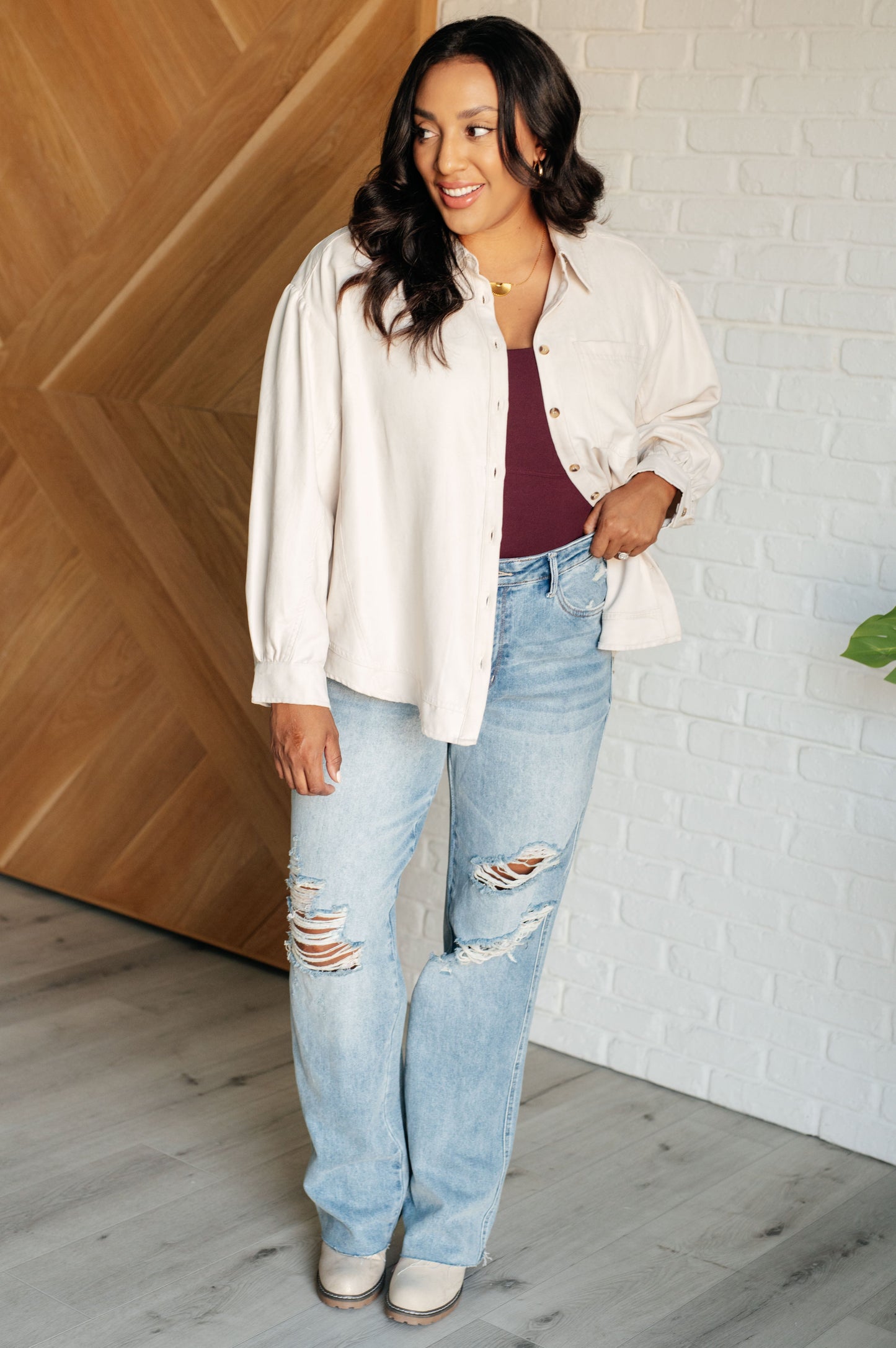 Beige faux suede blouse with a collared neckline, drop shoulders, and long bishop sleeves. Features a chest patch pocket, front button closures, banded sleeve cuffs, and a scooped vented hemline.