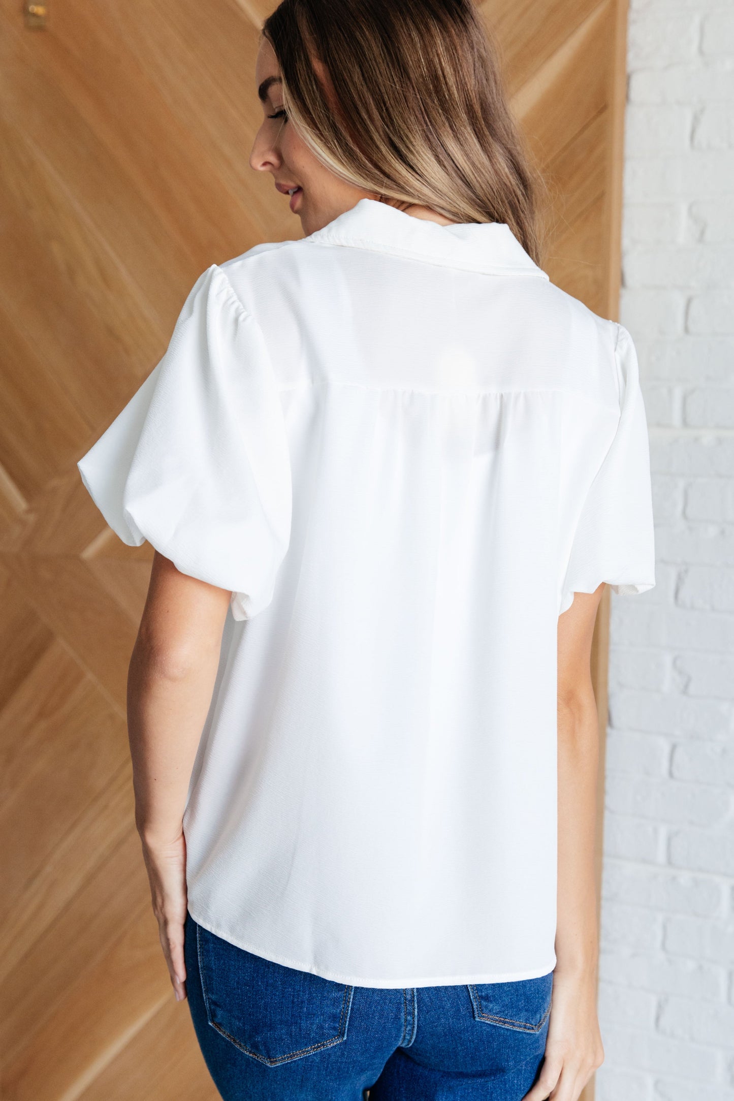 Women's white blouse with crinkle woven fabric, collared neckline, short balloon sleeves with elastic cuffs, and a front button closure.