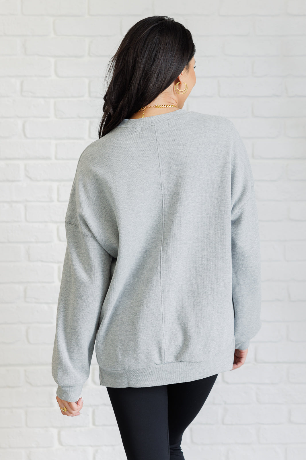 Oversized gray pullover in mid-weight knit with a banded crew neckline, drop shoulder long sleeves, banded cuffs and hemline, side slits, and back seam detail.