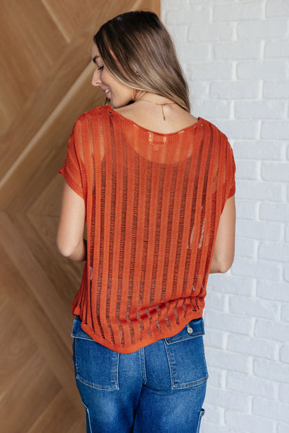 Back view of the Aaliyah Loose Knit Top in burnt orange with a wide v-neckline, short sleeves, and a lightweight open knit stripe pattern. A cozy and stylish sweater knit design.