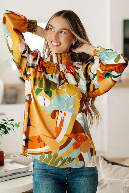 Front view of Dylan Mock Neck Blouse in tangerine base with multi-colored floral satin and smocked neckline