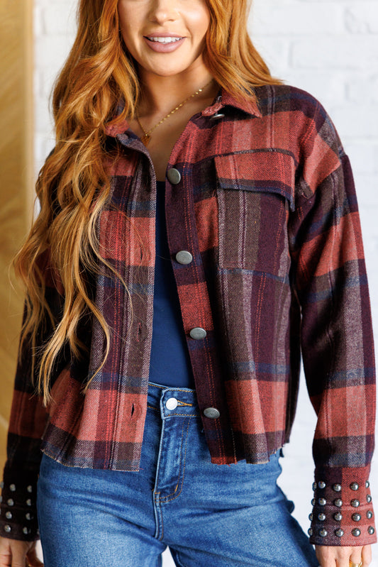 Plaid midweight flannel shacket with a collared neckline, long sleeves, studded sleeve cuffs, button closures, raw hem, and flap patch pockets.