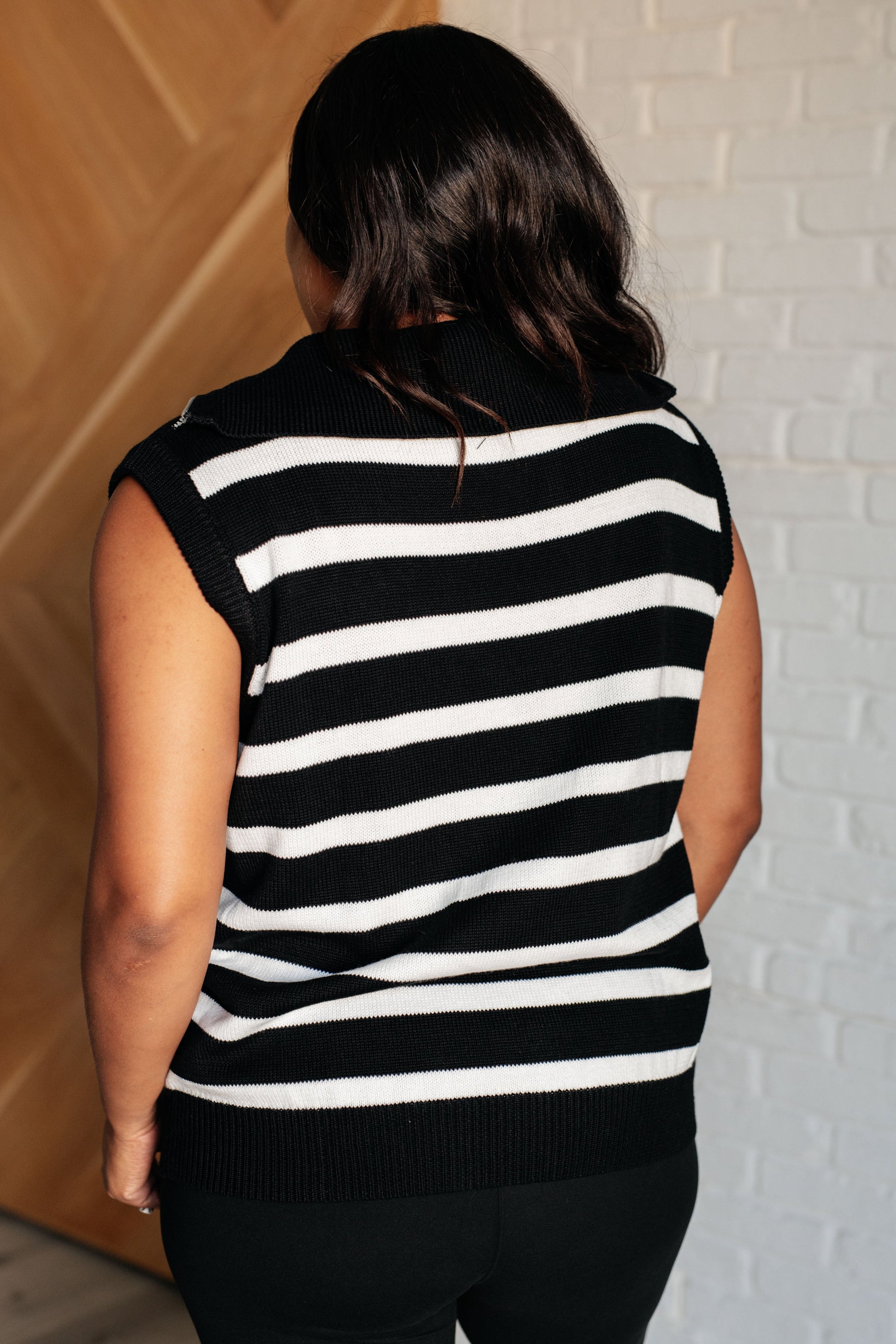 Black and white sleeveless sweater knit top featuring a striped pattern, a collared neckline, and a half-zip closure. It includes banded ribbed cuffs and a hemline for added detail.