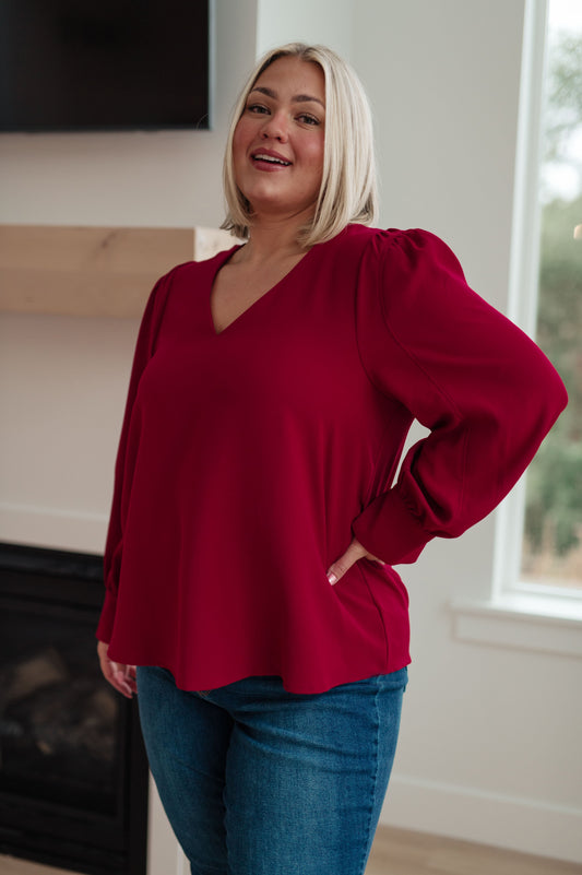 Wine-colored lightweight woven blouse with a V-neckline, long puff sleeves, and buttoned sleeve cuffs.