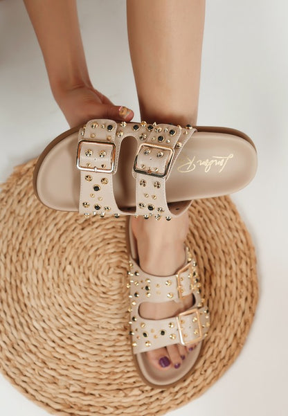 Beige studded slide sandals with pin buckle straps, open toe, and 1-inch platform heel.