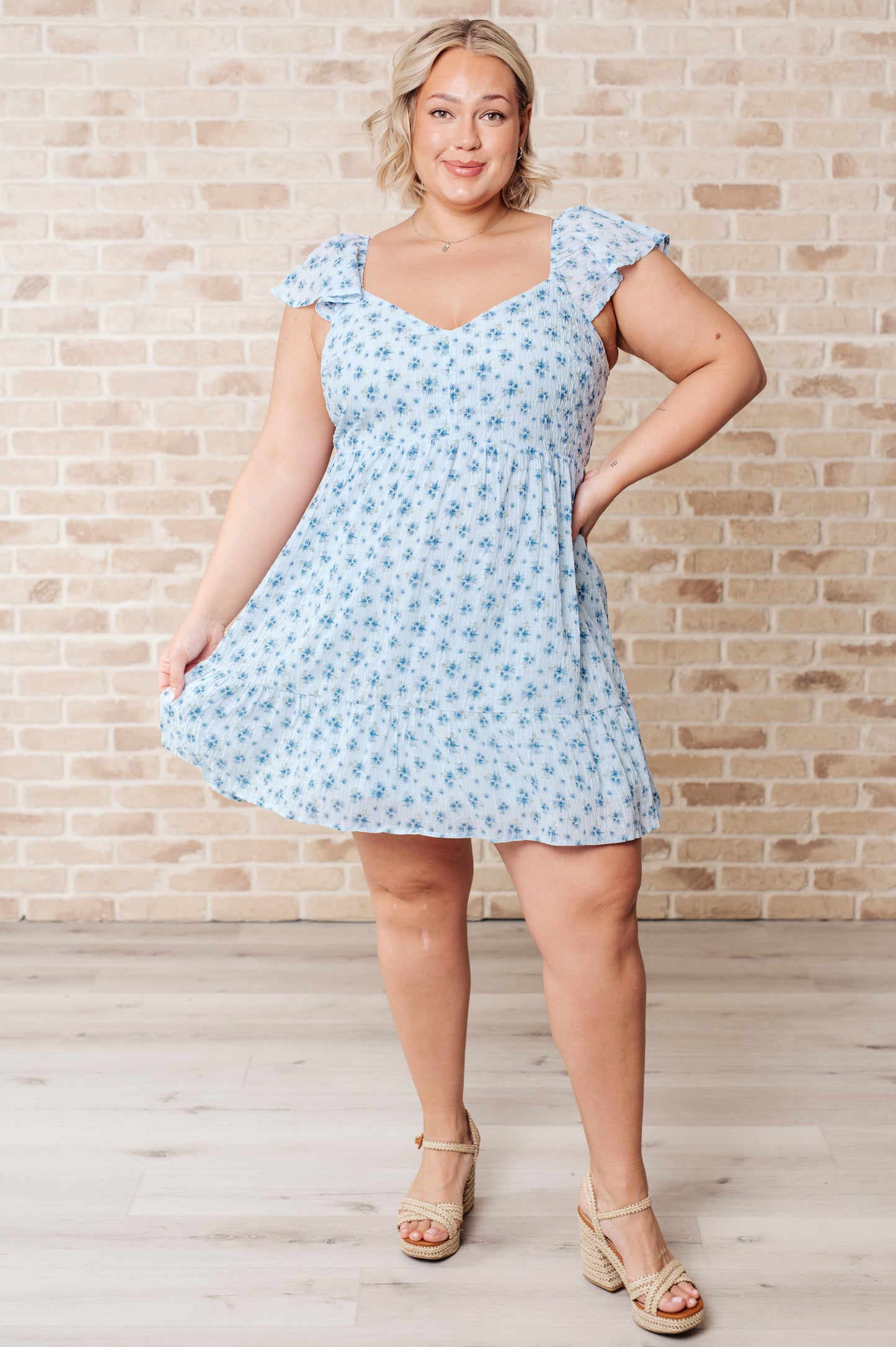 McKay V-Neck Floral Dress in blue with a playful floral print, featuring a flattering V-neckline, flutter sleeves, open back with a tie detail, and crinkle woven fabric for effortless charm. Fully lined for comfort, perfect for brunches, picnics, or special occasions.