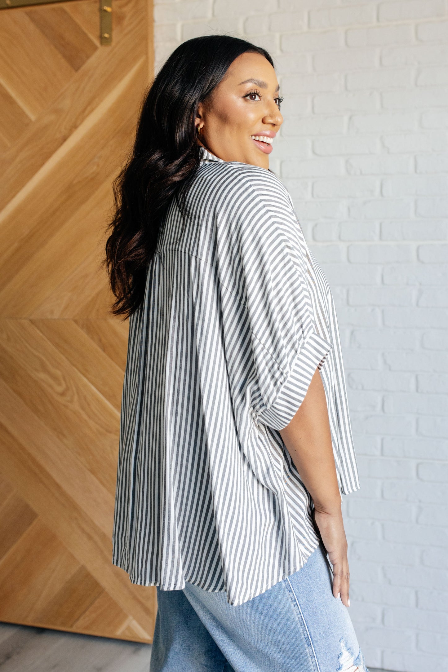 Side view of women's Plus SIze button-up shirt in  white with black stripes, featuring a collared neckline, short dolman sleeves, banded cuffs, button closure, and a scooped hemline.