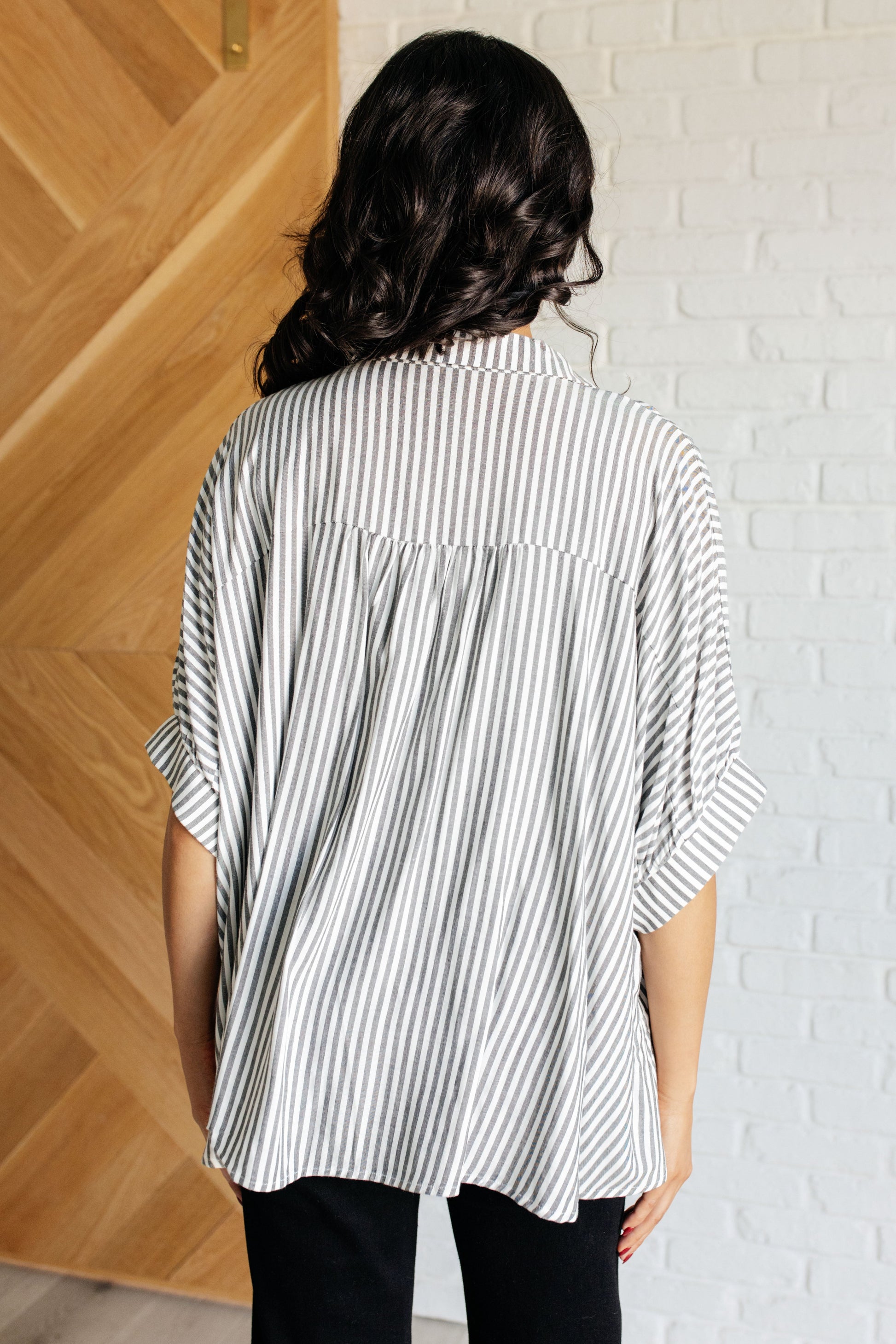 Back view of women's button-up shirt in  white with black stripes, featuring a collared neckline, short dolman sleeves, banded cuffs, button closure, and a scooped hemline.