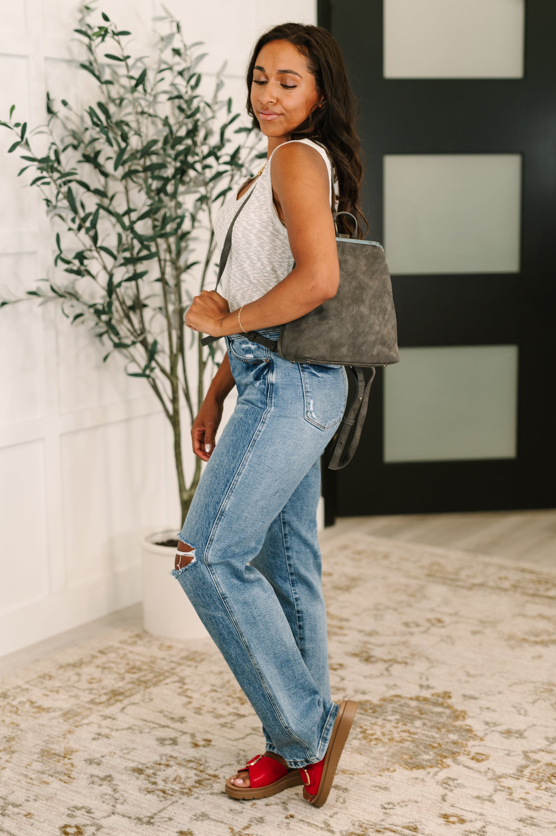 Woman holding the Bridget Mini Charcoal Backpack by one strap over her shoulder, showcasing hands-free styling option.