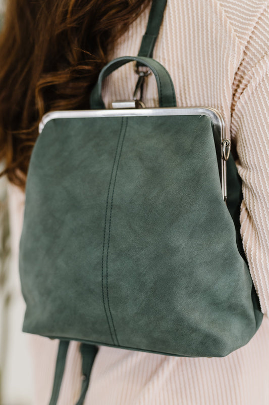 Model wearing Bridget Backpack in Peacock as backpack, vegan leather with brass clasp closure.