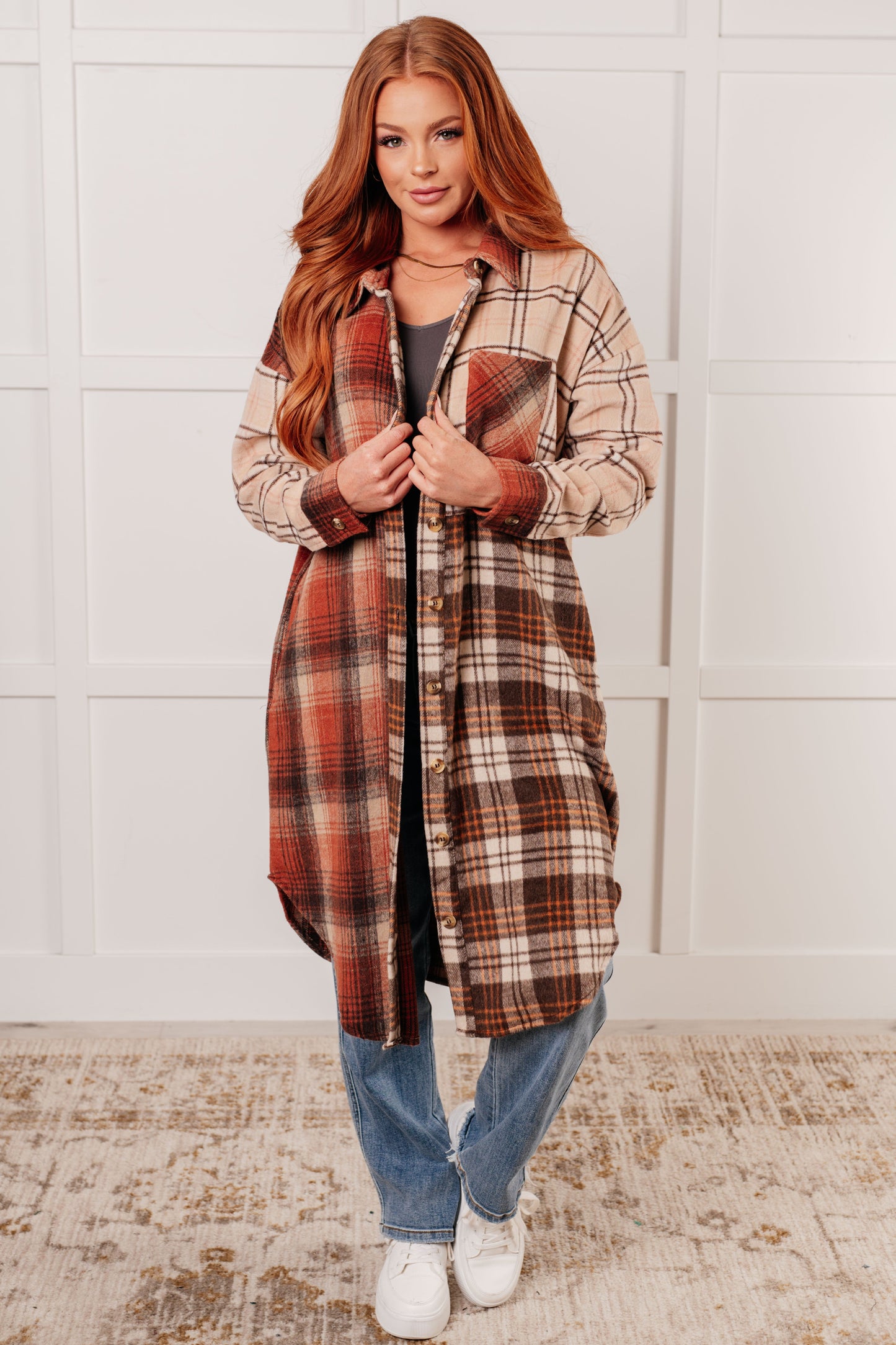 Oversized flannel shacket with a mixed plaid pattern in brown, orange, and beige. Features a collared neckline, drop shoulder design, button closures, functional side pockets, and a scooped hem.