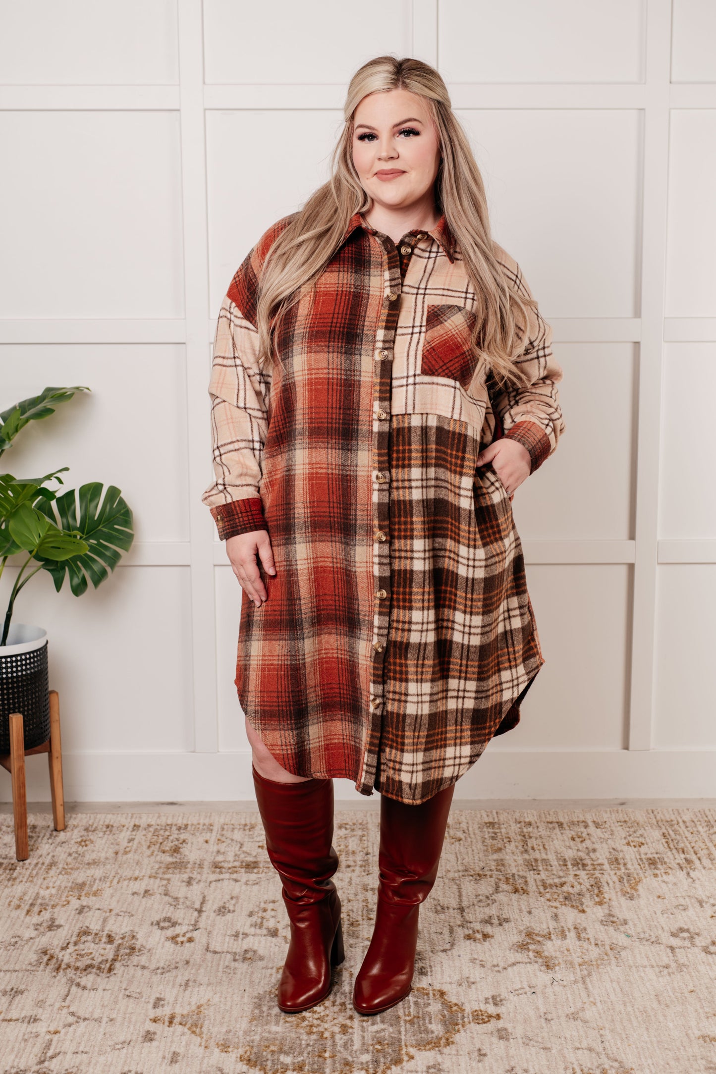 Oversized flannel shacket with a mixed plaid pattern in brown, orange, and beige. Features a collared neckline, drop shoulder design, button closures, functional side pockets, and a scooped hem.