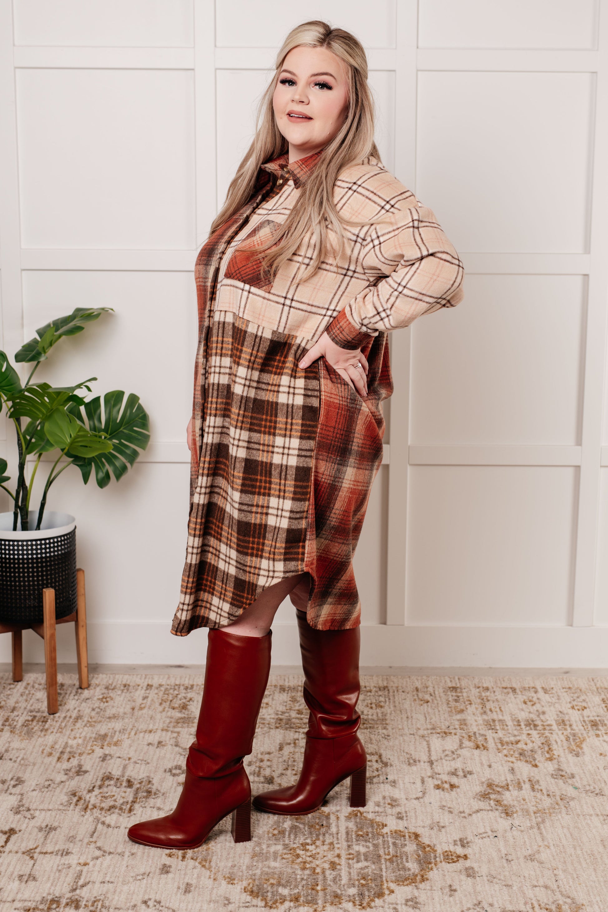 Oversized flannel shacket with a mixed plaid pattern in brown, orange, and beige. Features a collared neckline, drop shoulder design, button closures, functional side pockets, and a scooped hem.