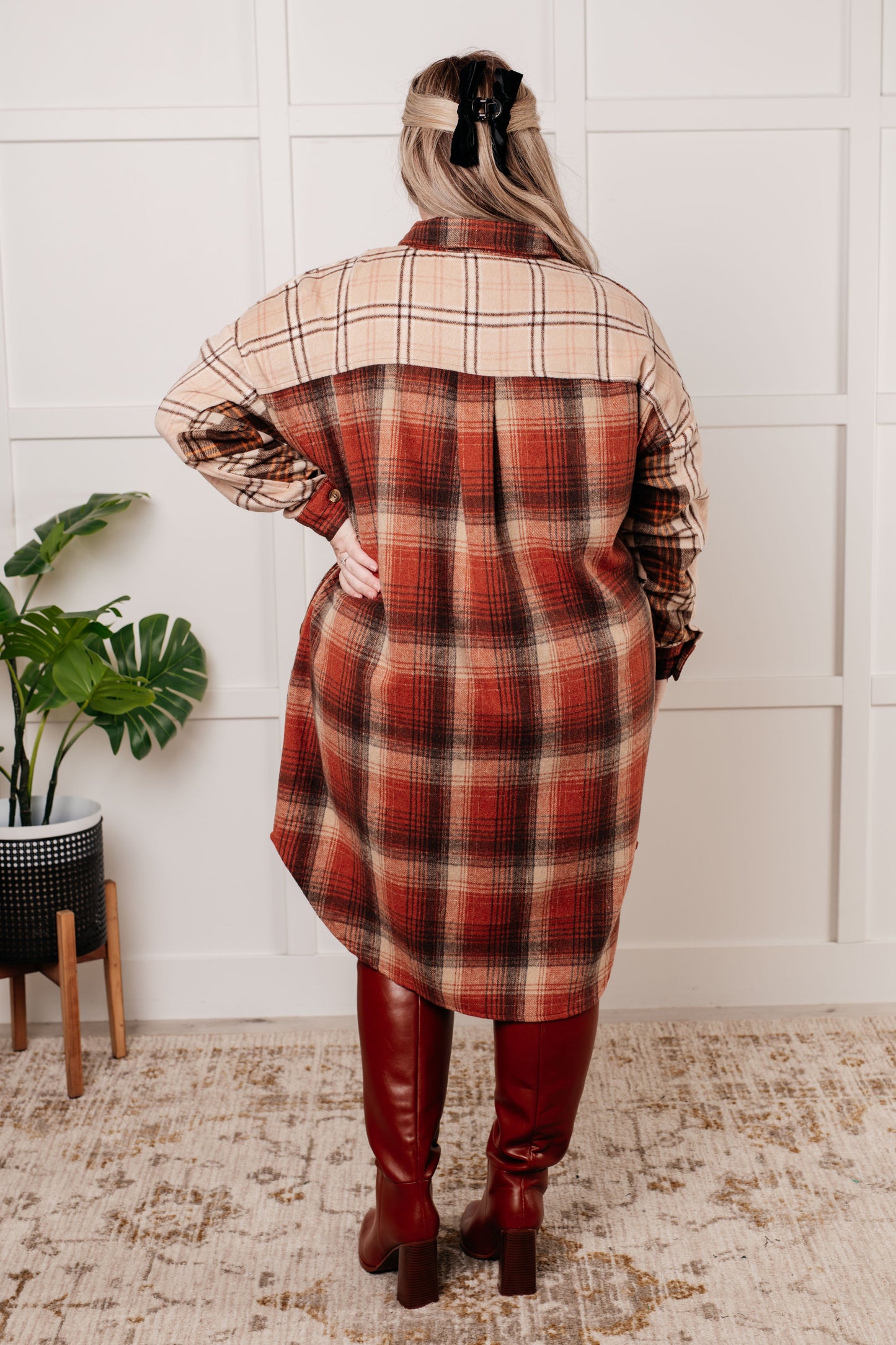 Oversized flannel shacket with a mixed plaid pattern in brown, orange, and beige. Features a collared neckline, drop shoulder design, button closures, functional side pockets, and a scooped hem.