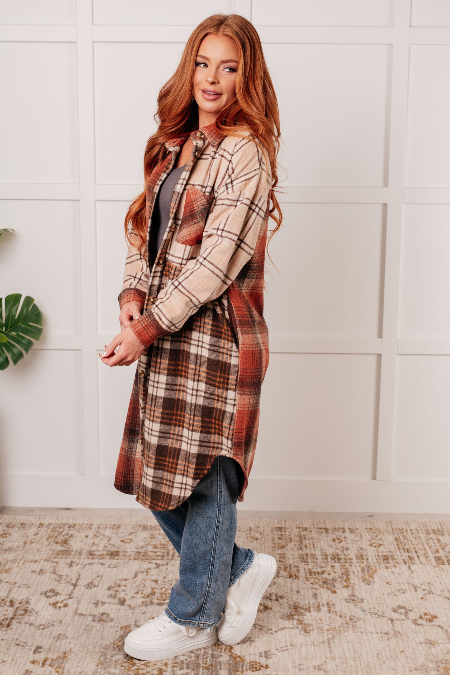 Oversized flannel shacket with a mixed plaid pattern in brown, orange, and beige. Features a collared neckline, drop shoulder design, button closures, functional side pockets, and a scooped hem.