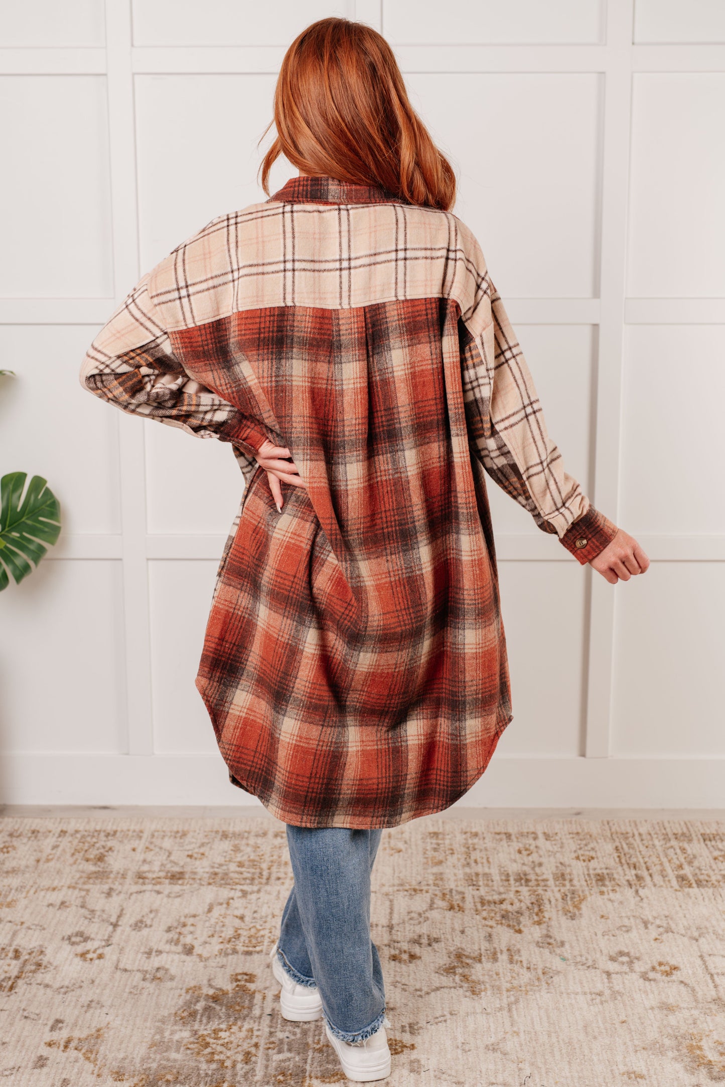 Oversized flannel shacket with a mixed plaid pattern in brown, orange, and beige. Features a collared neckline, drop shoulder design, button closures, functional side pockets, and a scooped hem.