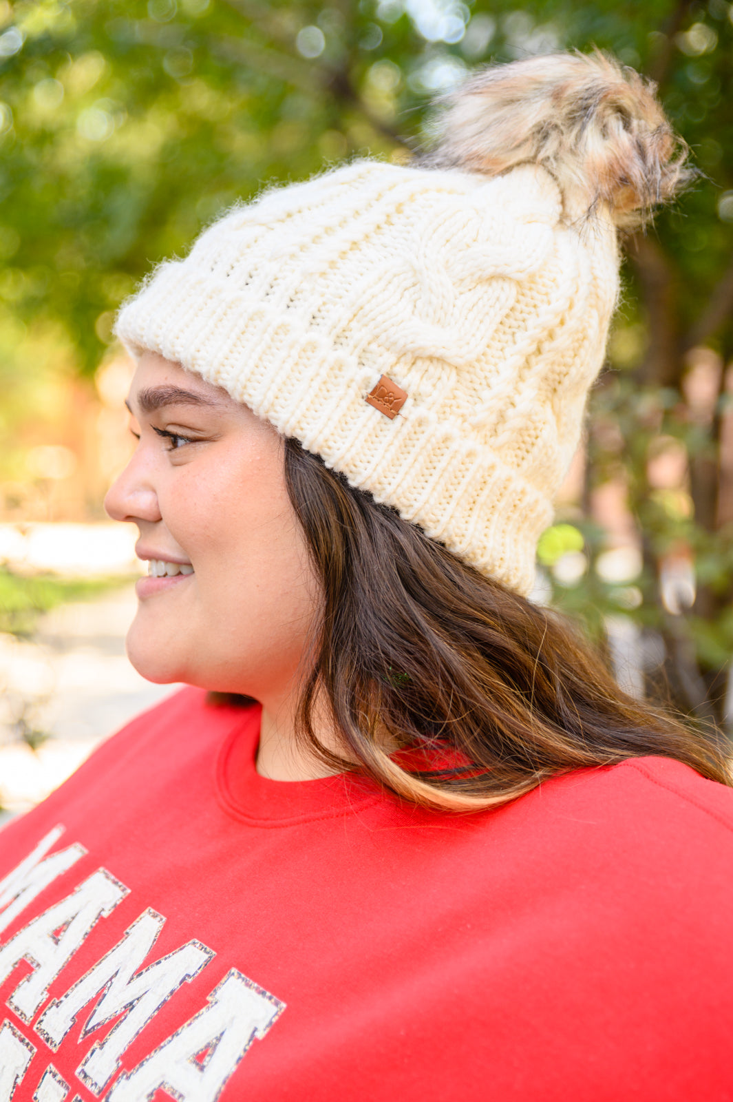 Ivory cable knit beanie with a pom top, cuffed hem, and fuzzy lining for warmth.