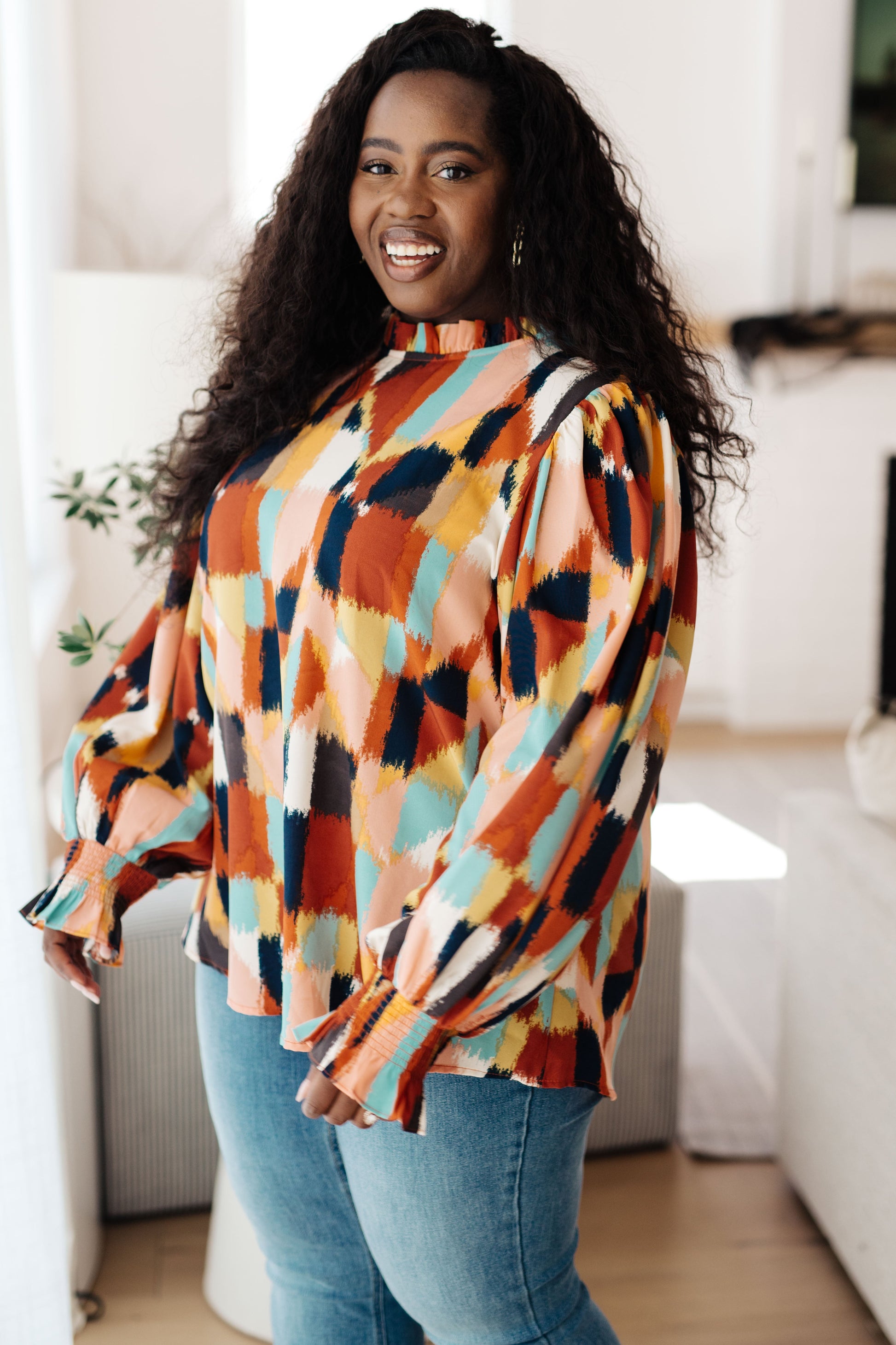 Side view of plus size modeal wearing the Padme Blouse featuring a bold mod print, ruffled neckline, and smocked elastic sleeve cuffs for a chic, vintage-inspired look with a modern twist.