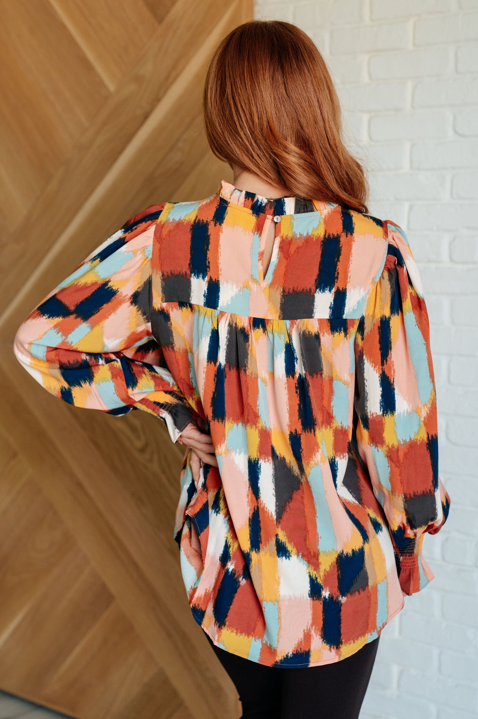 Back view of the Padme Blouse featuring a bold mod print, ruffled neckline, and smocked elastic sleeve cuffs for a chic, vintage-inspired look with a modern twist.