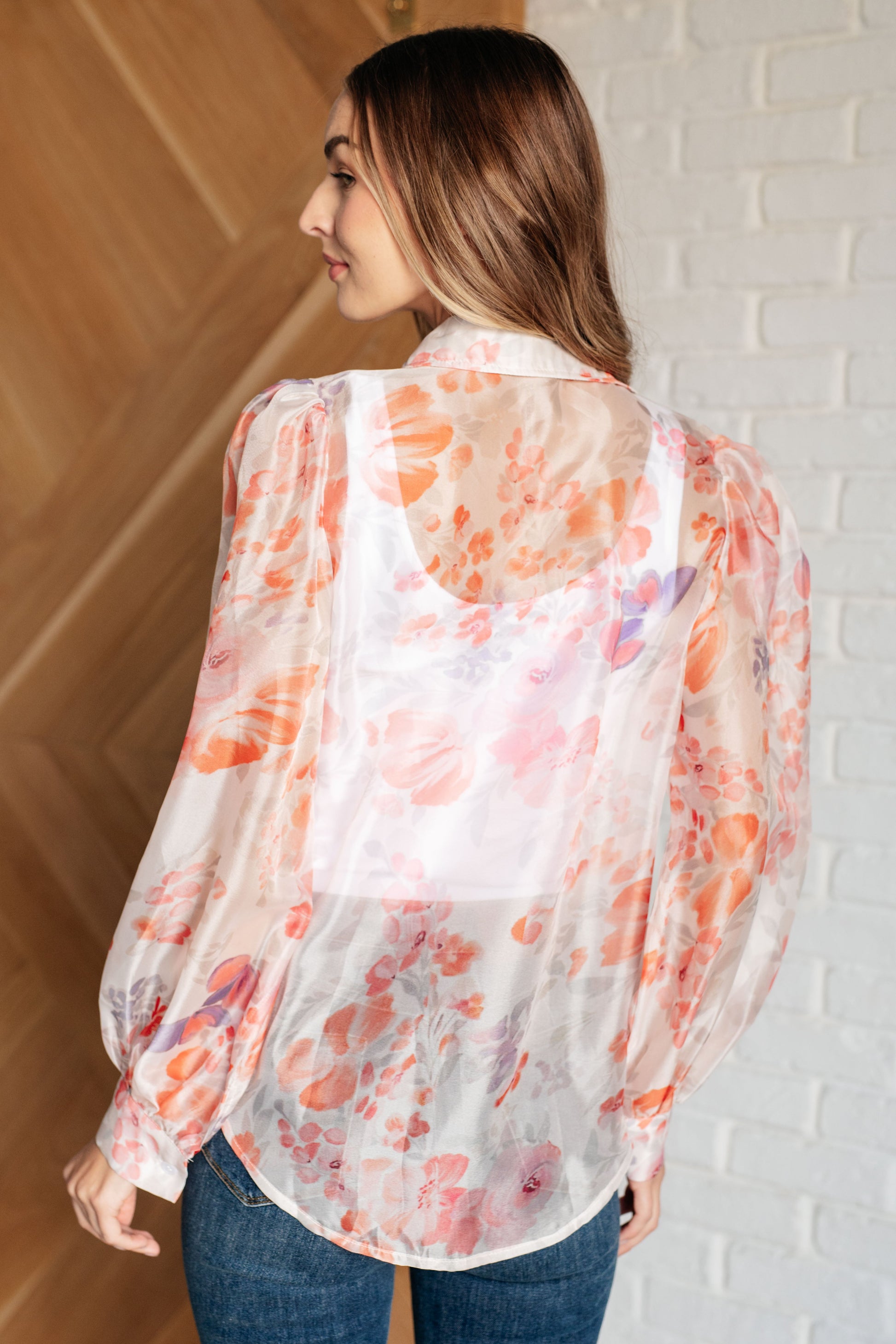 A floral sheer blouse with a collared neckline, long sleeves, and button closure. It has a scooped high-low hem and gathered shoulders.