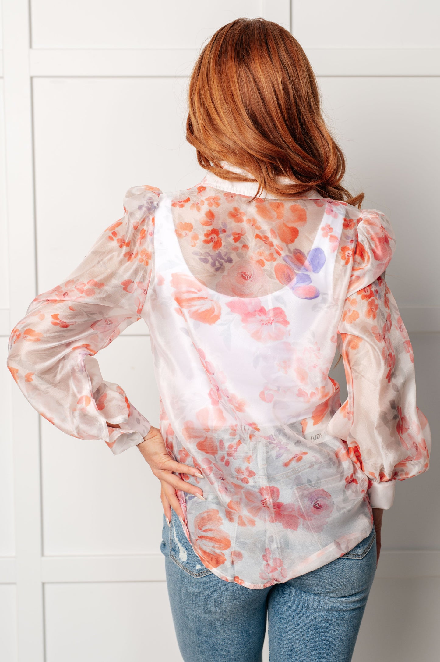 A floral sheer blouse with a collared neckline, long sleeves, and button closure. It has a scooped high-low hem and gathered shoulders.