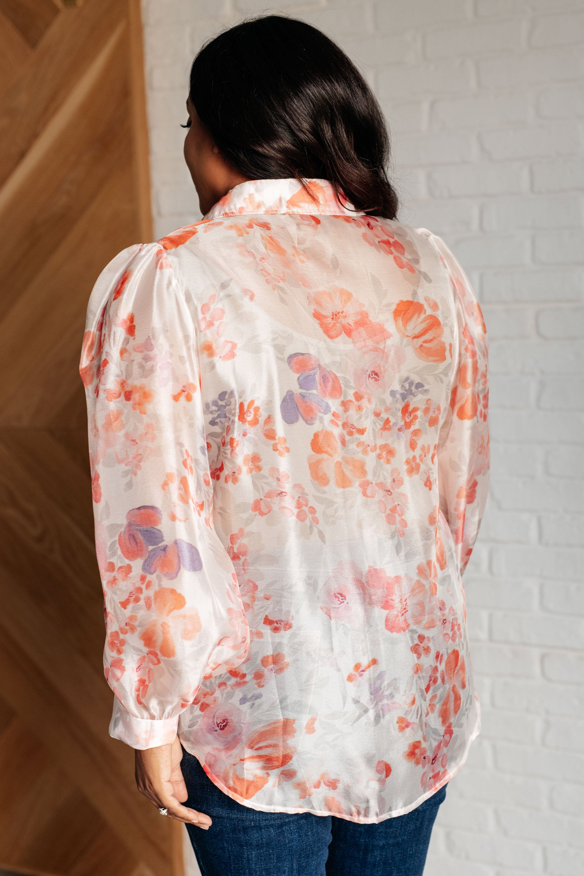 A floral sheer blouse with a collared neckline, long sleeves, and button closure. It has a scooped high-low hem and gathered shoulders.