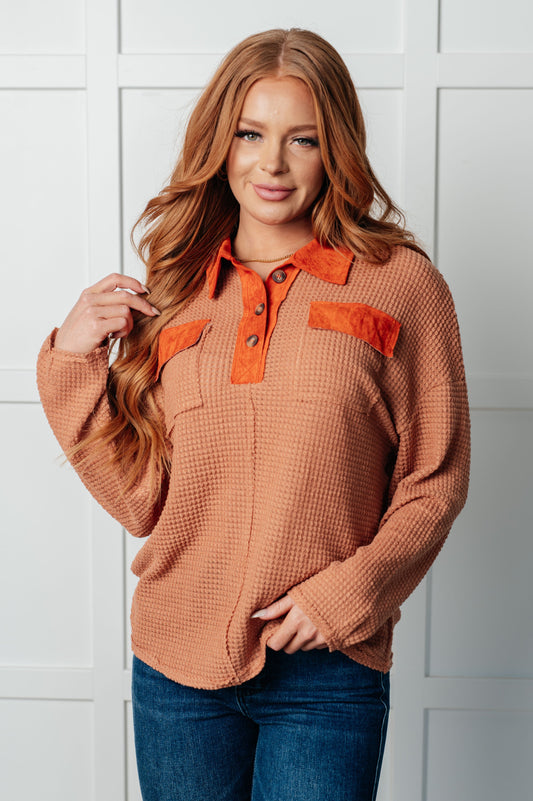 Cozy pumpkin-colored top with waffle knit fabric, faux suede contrast trim, collared neckline, drop shoulder, half front button closure, functional chest patch pockets, and raw seam details.