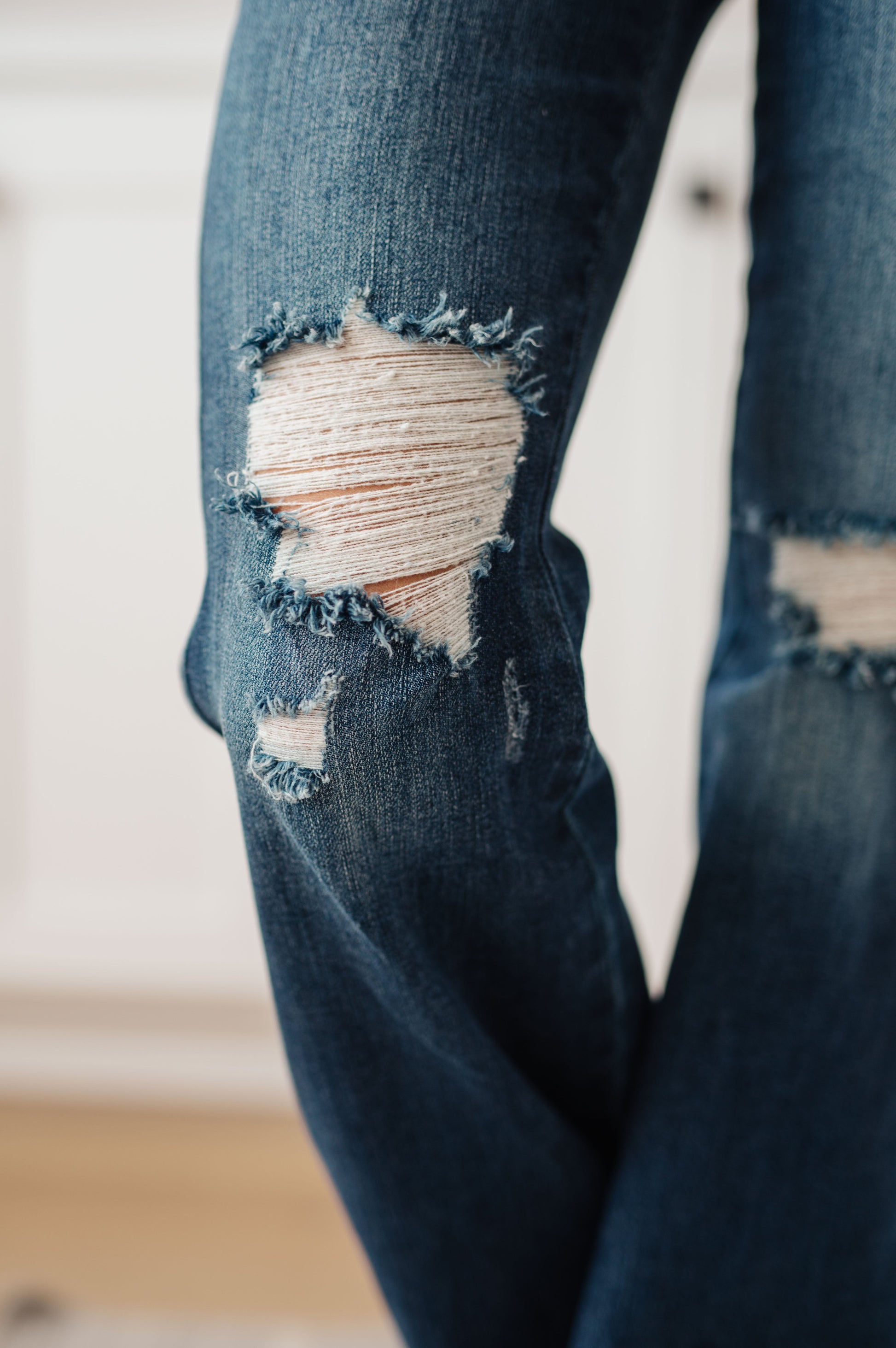 Dark wash high-rise jeans with a flared silhouette, distressed details, and a raw hem. Features tummy control technology, a zip fly closure, and 4-way stretch.