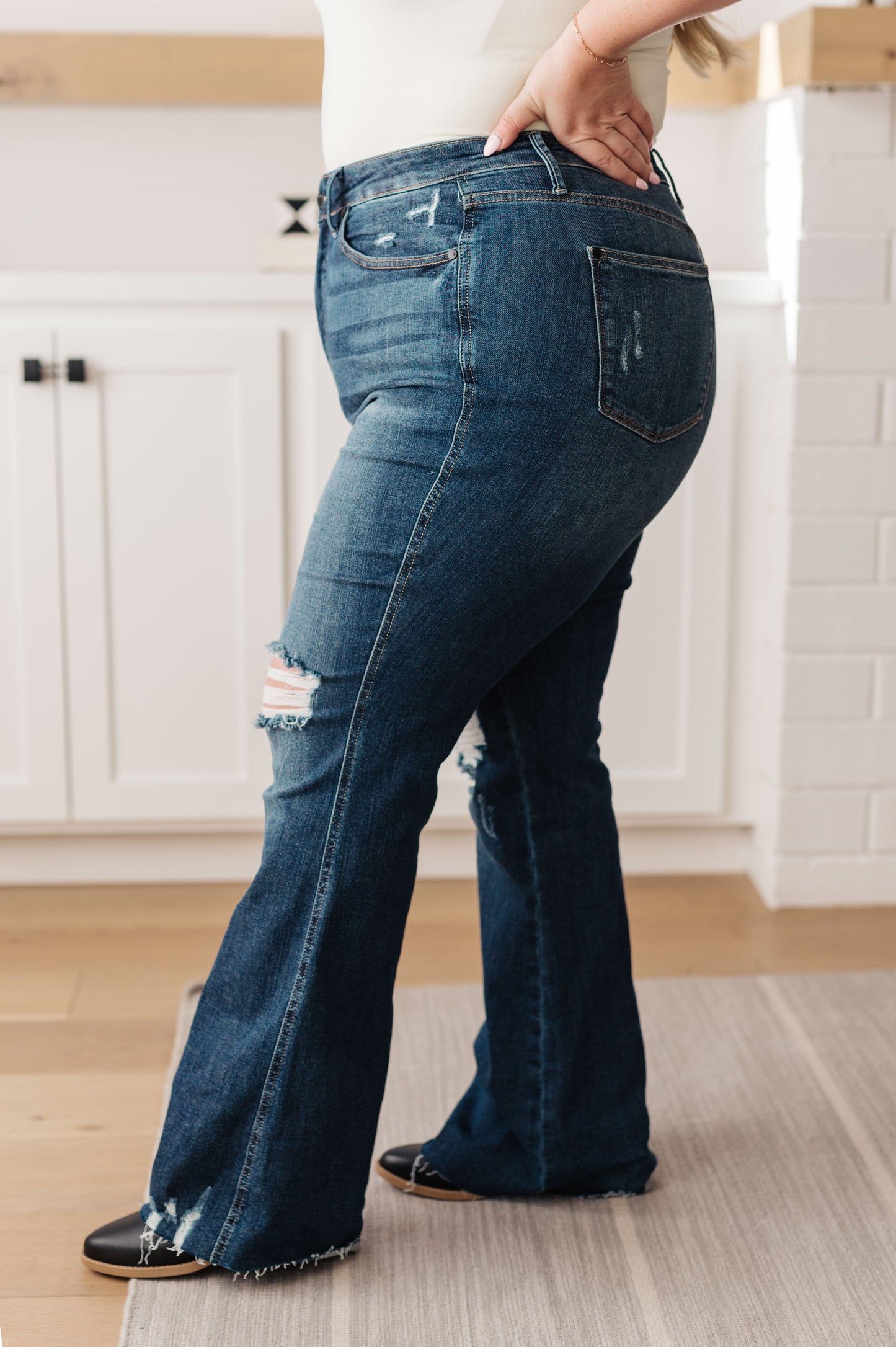 Dark wash high-rise jeans with a flared silhouette, distressed details, and a raw hem. Features tummy control technology, a zip fly closure, and 4-way stretch.