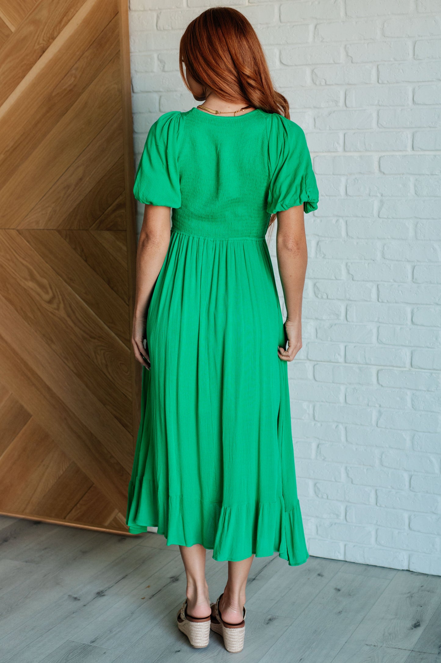 Green smocked dress with a V-neckline, short balloon sleeves, and a ruffled hemline.