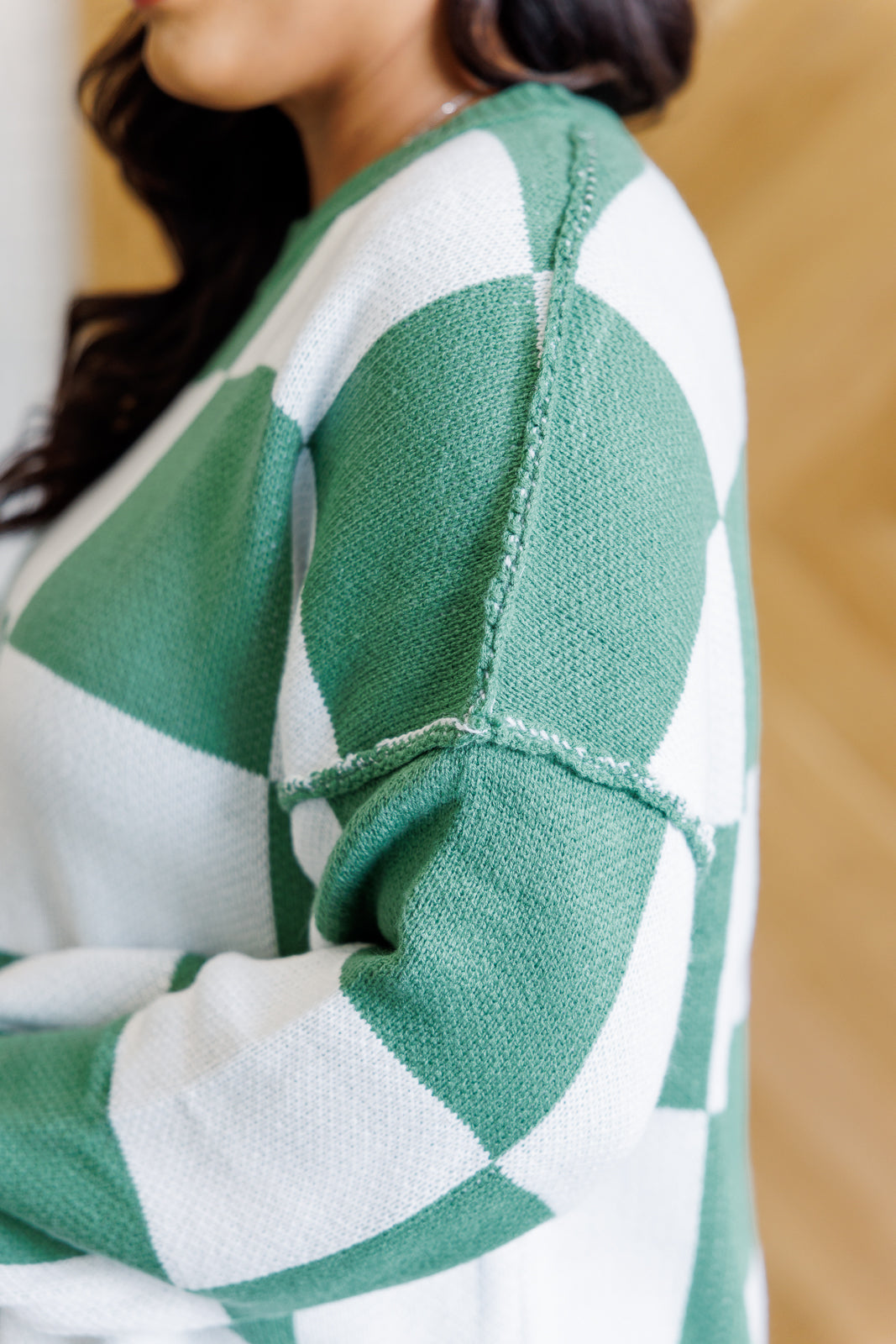 A women's green and white checkered sweater with a round neckline, long sleeves with drop shoulders, exaggerated ribbed cuffs, exposed seam, and a banded ribbed hemline.