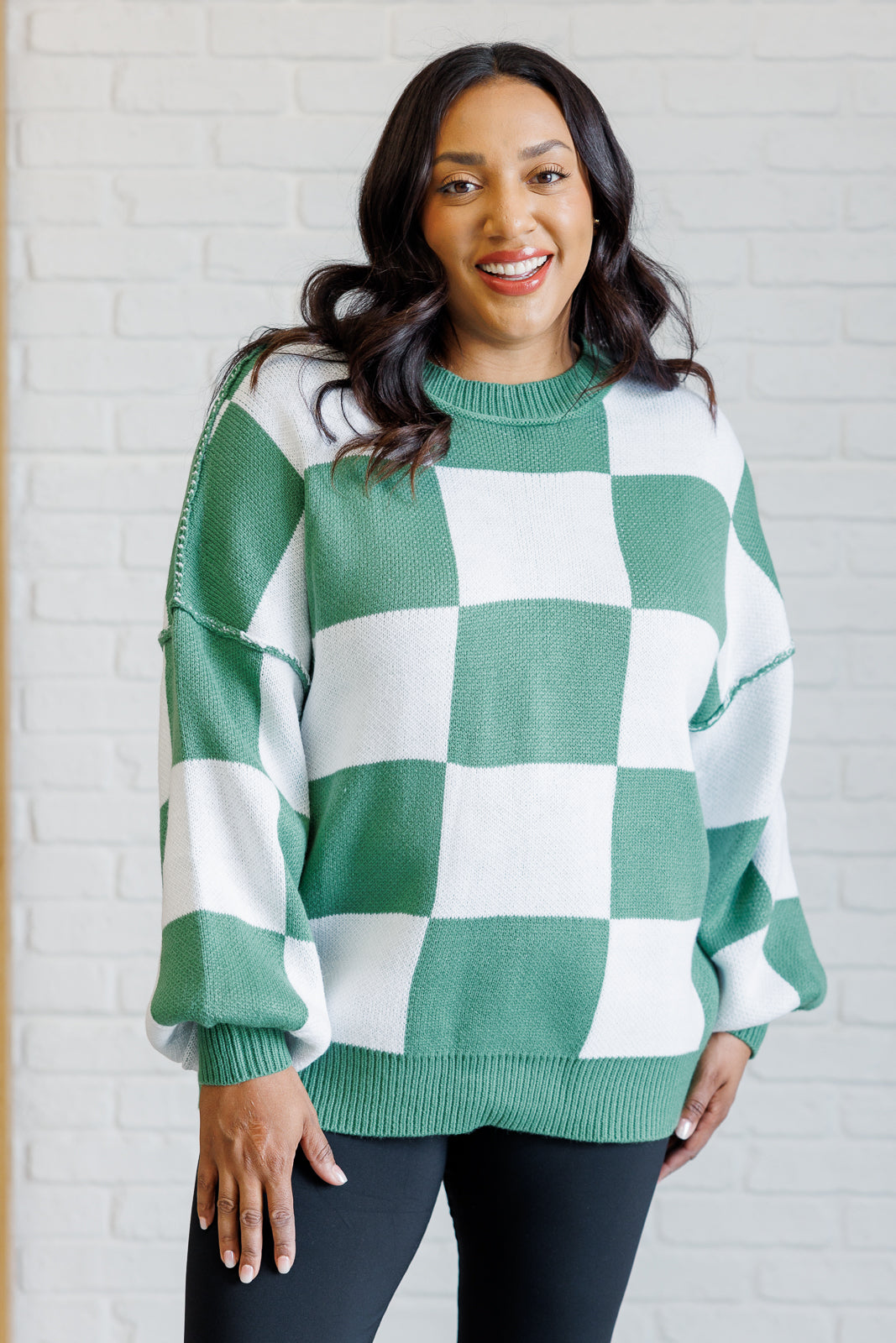 A women's green and white checkered sweater with a round neckline, long sleeves with drop shoulders, exaggerated ribbed cuffs, exposed seam, and a banded ribbed hemline.