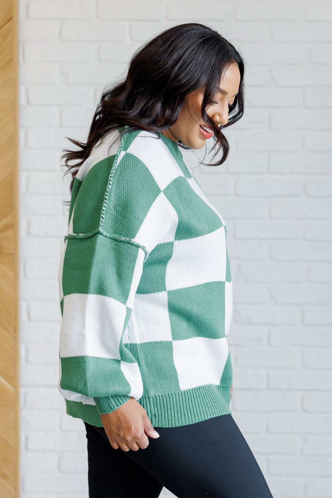 A women's green and white checkered sweater with a round neckline, long sleeves with drop shoulders, exaggerated ribbed cuffs, exposed seam, and a banded ribbed hemline.