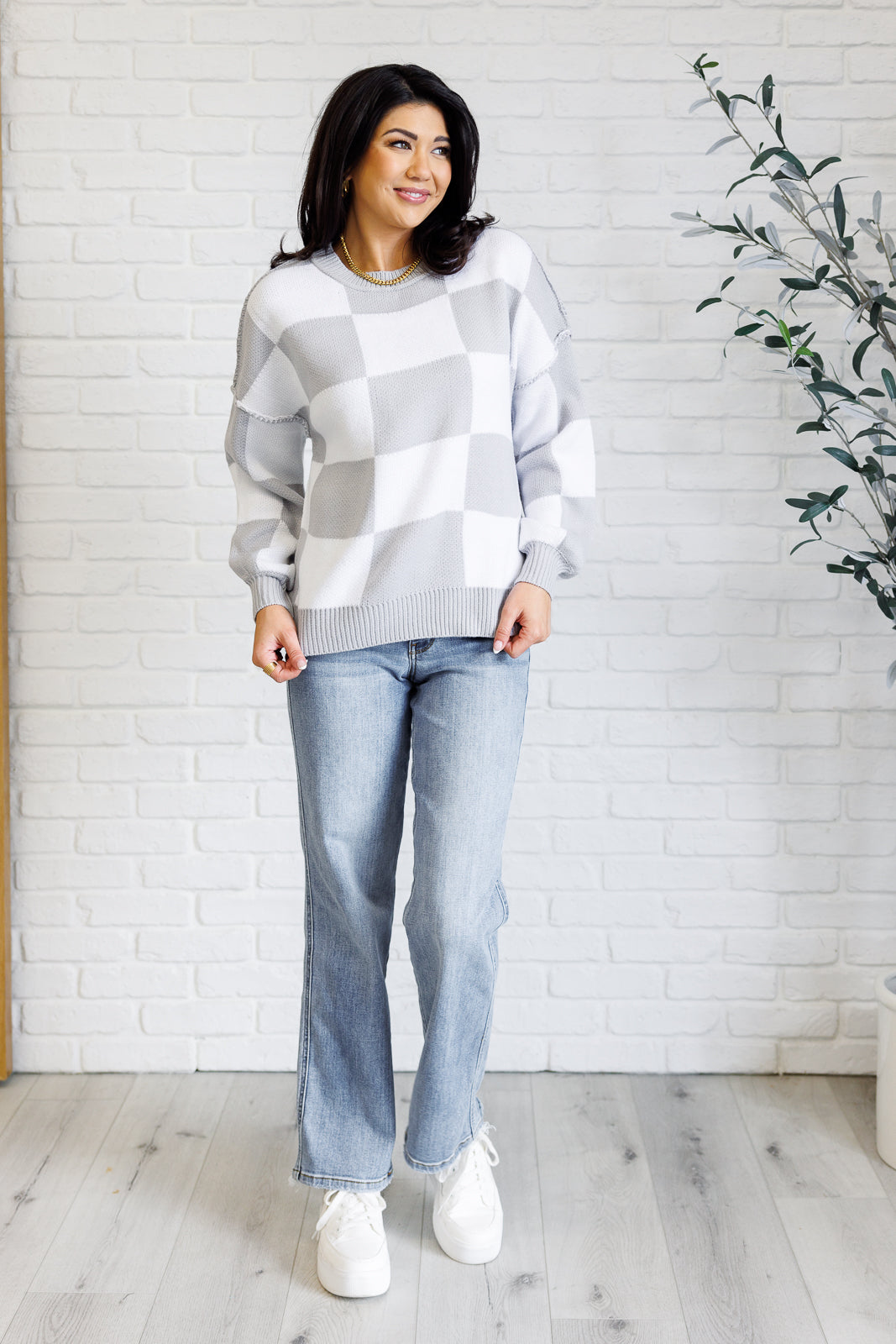 A women's gray and white checkered sweater with a round neckline, long sleeves with drop shoulders, exaggerated ribbed cuffs, exposed seam details, and a banded ribbed hemline.