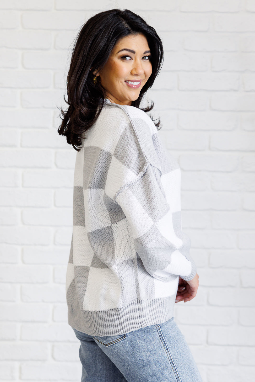 A women's gray and white checkered sweater with a round neckline, long sleeves with drop shoulders, exaggerated ribbed cuffs, exposed seam details, and a banded ribbed hemline.