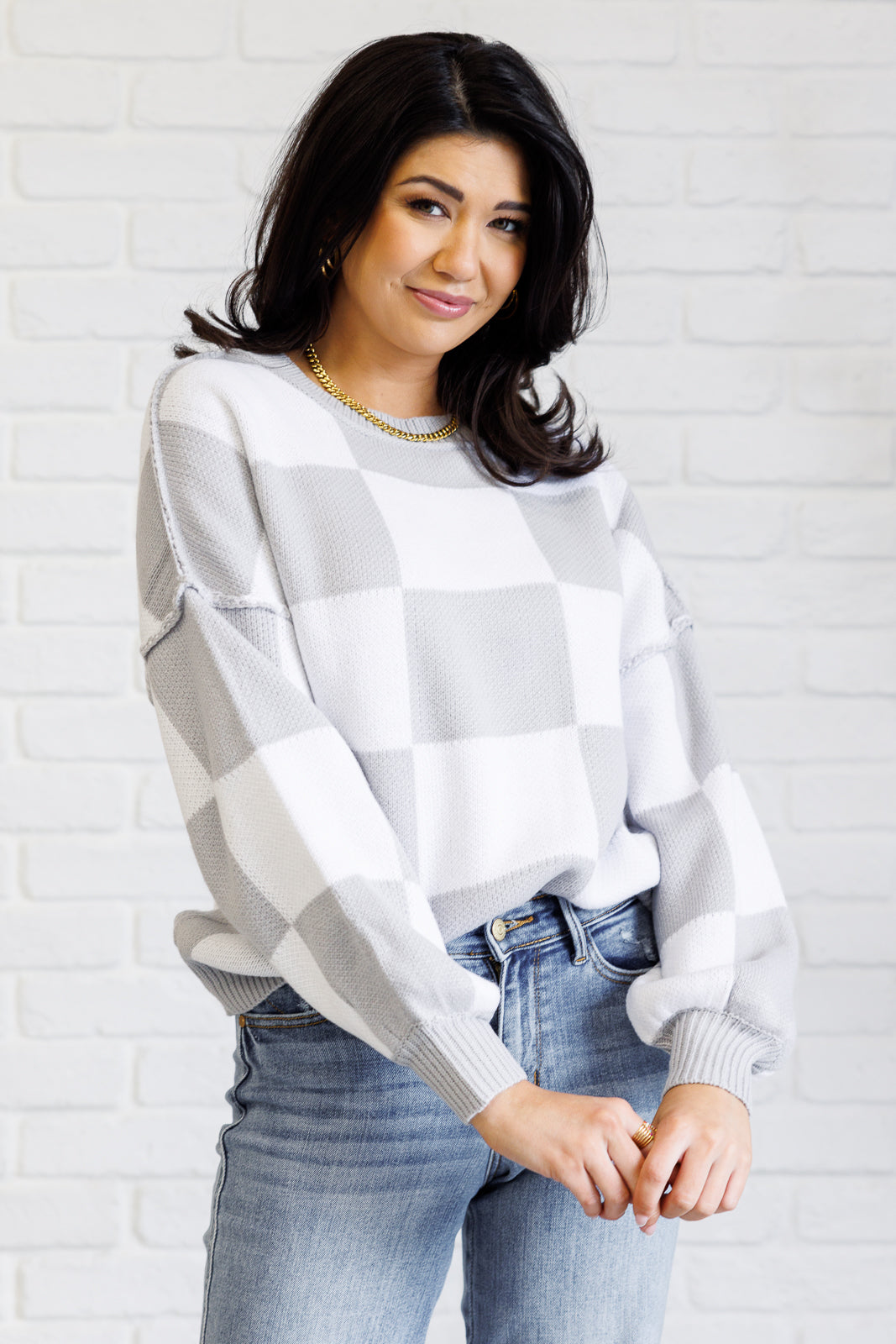 A women's gray and white checkered sweater with a round neckline, long sleeves with drop shoulders, exaggerated ribbed cuffs, exposed seam details, and a banded ribbed hemline.