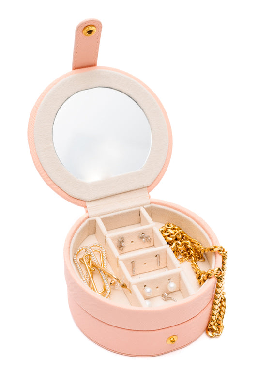 Circular Travel Jewelry Case in pink, with secure snap closure, small mirror, six ring slots, four perforated sections for earrings, six compartments for jewelry, and three necklace hooks.