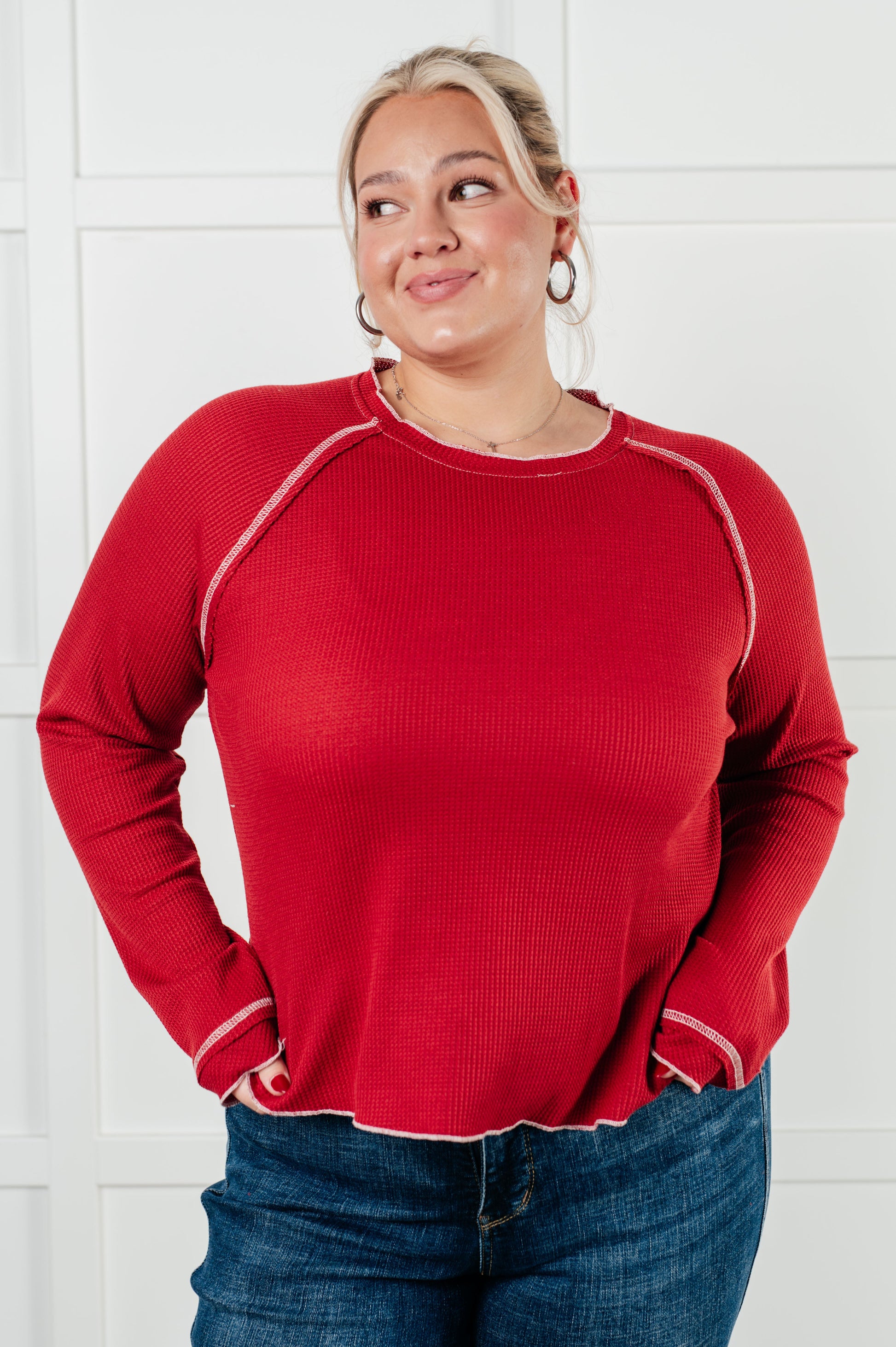 Red waffle knit top with raglan sleeves, exposed seams, and contrast stitching for a stylish and comfortable look. Features raw edges and light stretch.