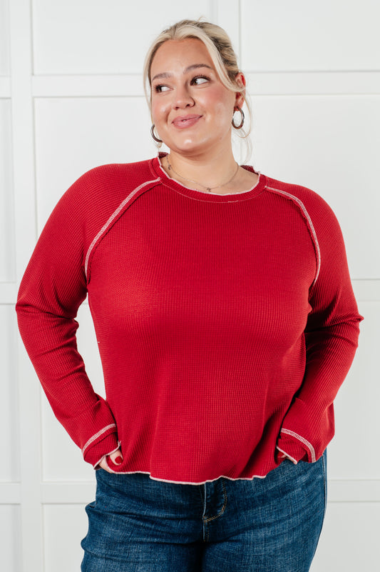 Red waffle knit top with raglan sleeves, exposed seams, and contrast stitching for a stylish and comfortable look. Features raw edges and light stretch.