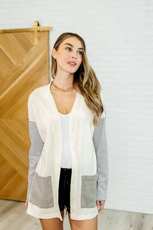 Front view of woman wearing the Evie Gray Color Block Cardigan with cream accents and black-and-white striped sleeves and pockets, featuring an open front and drop shoulder design.